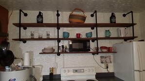 Una cocina con estantes de madera que sostienen diversos utensilios, un microondas y una estufa.