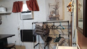 Cocina compacta con encimera de madera, un perchero con ropa y una ventana con cortinas.
