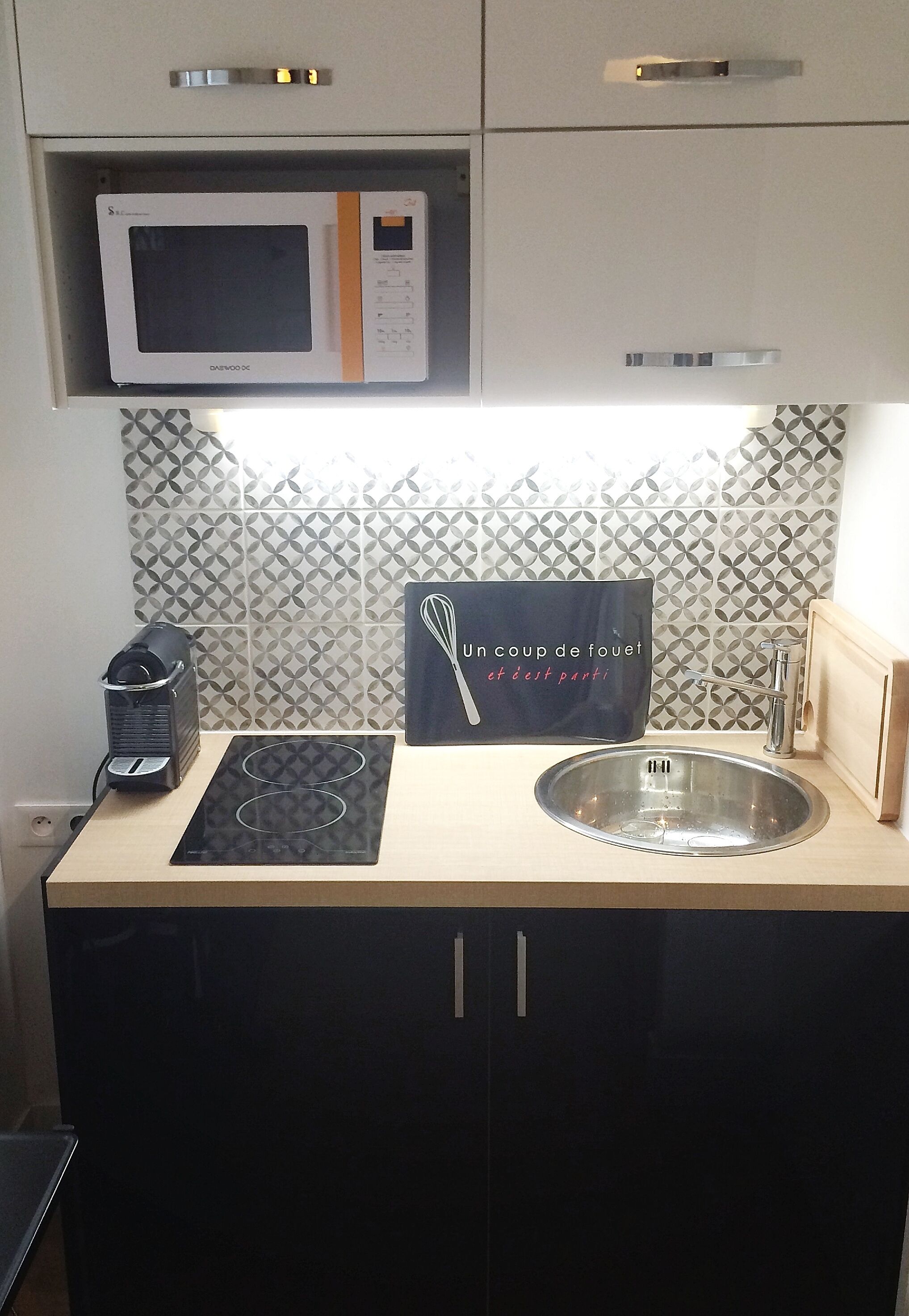 Una cucina con forno a microonde, macchina del caffè, lavello e un cartello decorativo.