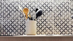 A kitchen with a patterned backsplash, a utensil holder, and cabinets.