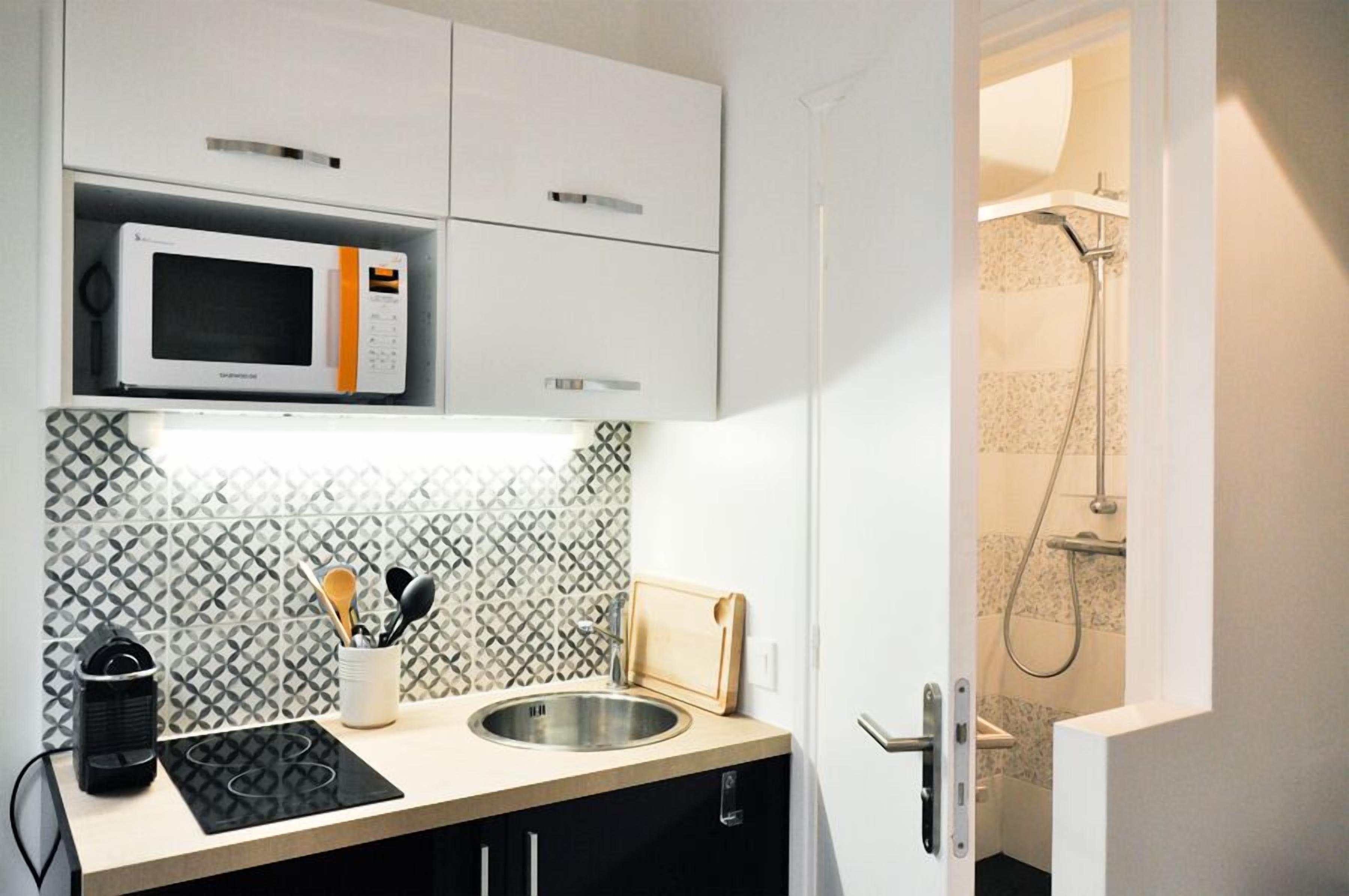 Een moderne keuken met een magnetron, spoelbak en houten snijplank.