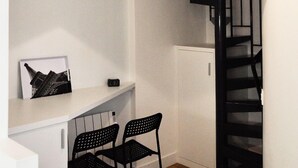 A modern kitchen with a white countertop, two black chairs, and a black staircase.