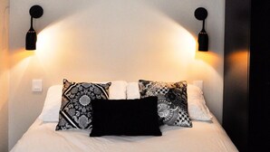 A neatly made bed with patterned pillows and two wall-mounted lamps on either side.