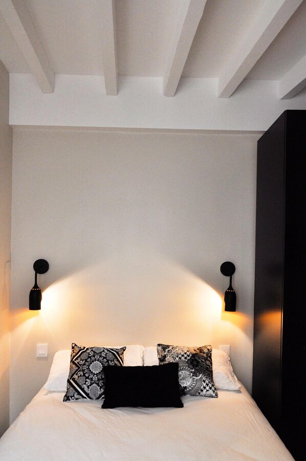 Una cama bien hecha con almohadones estampados y dos lámparas de pared a cada lado.