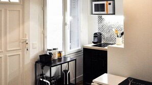 A compact kitchen with a microwave, a small countertop, and a cart with bags.