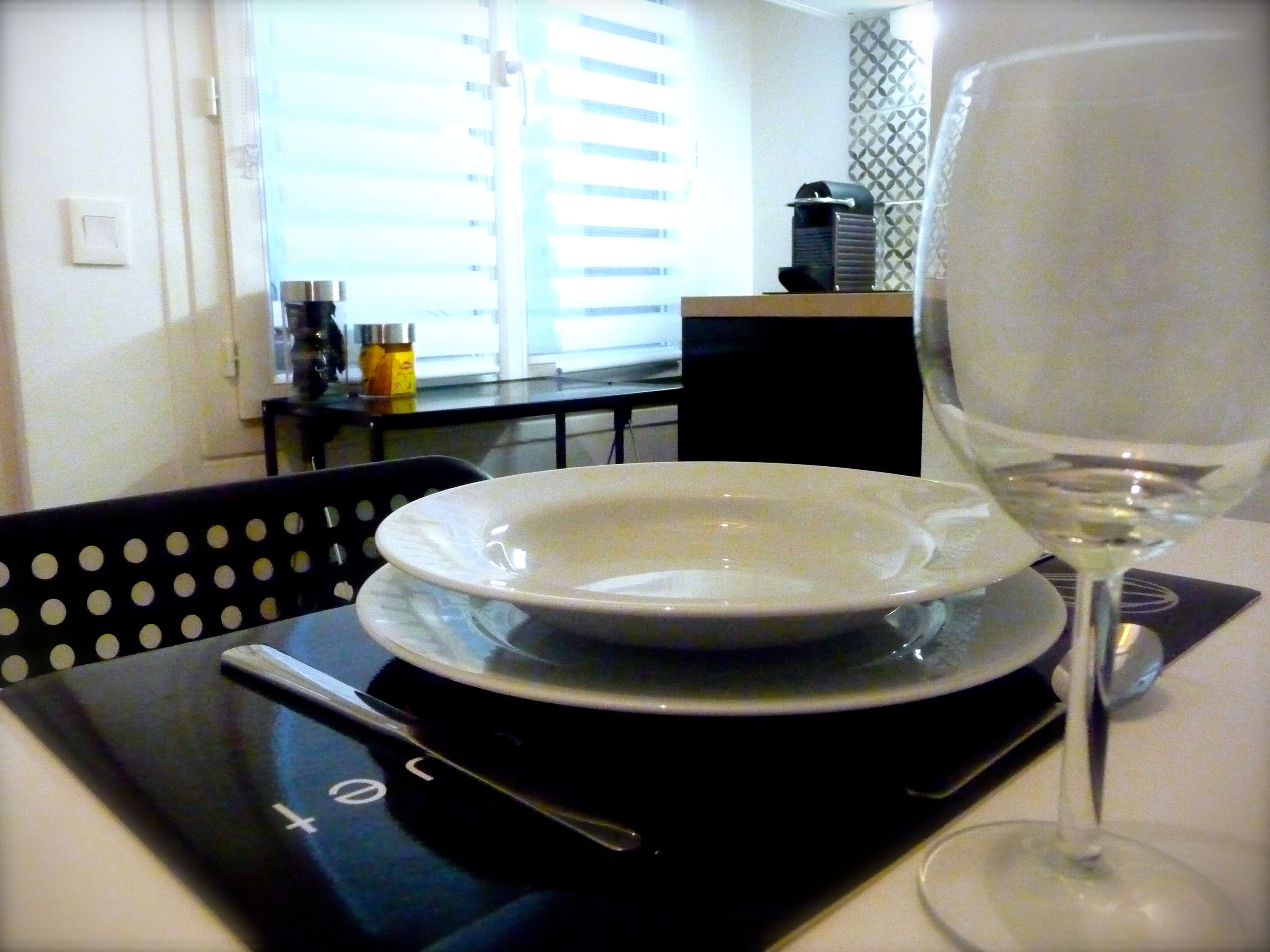 Une table à manger avec une assiette blanche, un verre à vin et une nappe noire agrémentée d’une cuillère.