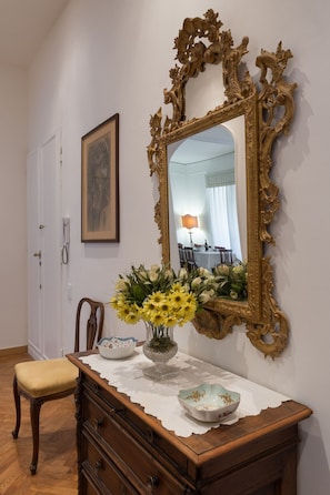 A room with a wooden dresser, a mirror with an ornate frame, a vase with flowers, and a framed picture on the wall.