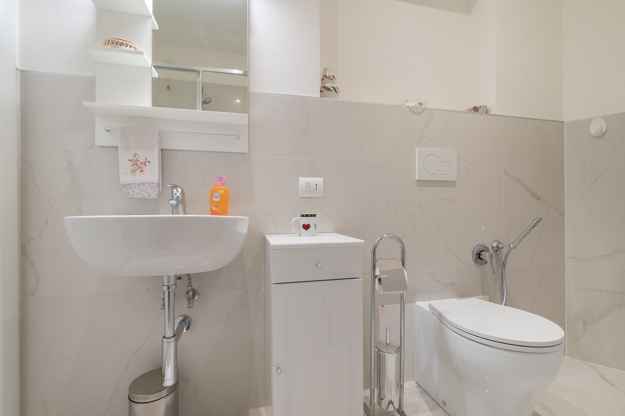 Een moderne badkamer met een witte wastafel, toilet en douche.