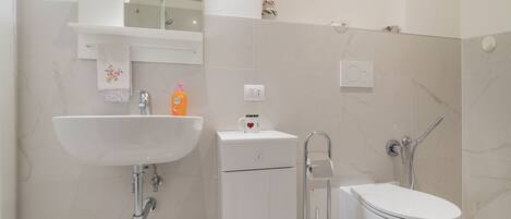 Een moderne badkamer met een witte wastafel, toilet en douche.