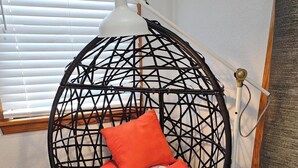 Ein Zimmer mit einem runden, schwarzen Hängekorbstuhl mit geometrischem Muster und einer weißen Lampe daneben.