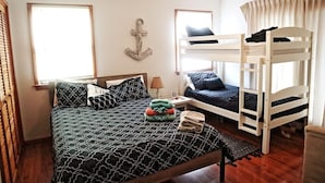 Een kamer met een enkel bed, een stapelbed, een houten vloer, een plafondventilator en een raam met gordijnen.