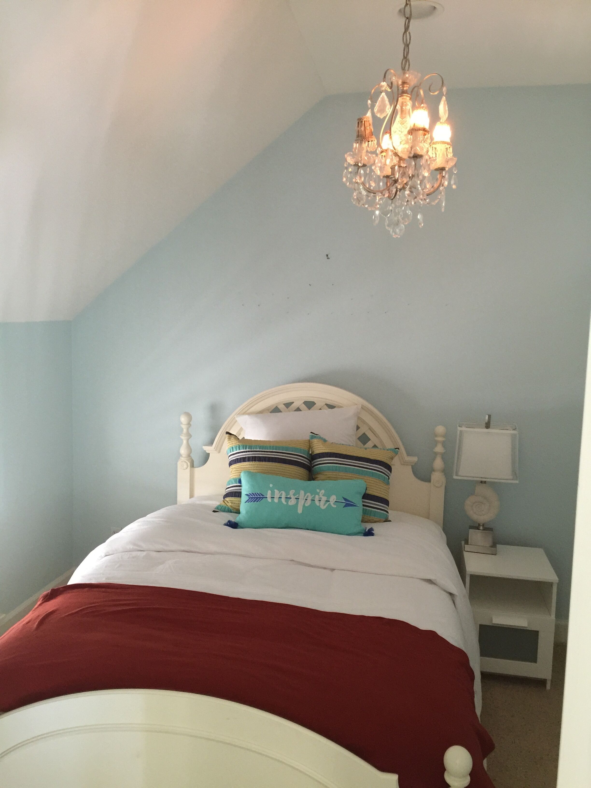 Un dormitorio con una cama blanca, un edredón rojo y una araña.