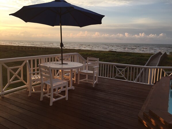 A wooden deck with a table and chairs, an umbrella, and a view of the ocean. - Amazing Pool & Private Beach: Free HS WiFi & Sleeps 10 w6 night min+ ESVE outlet (Galveston)