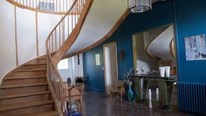 Un escalier en colimaçon avec des rampes en bois, un coin repas avec une table et des chaises, et un mur bleu orné d’un miroir.