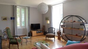 Un salon comprenant un téléviseur, deux fauteuils, un canapé, une table basse et une bibliothèque.