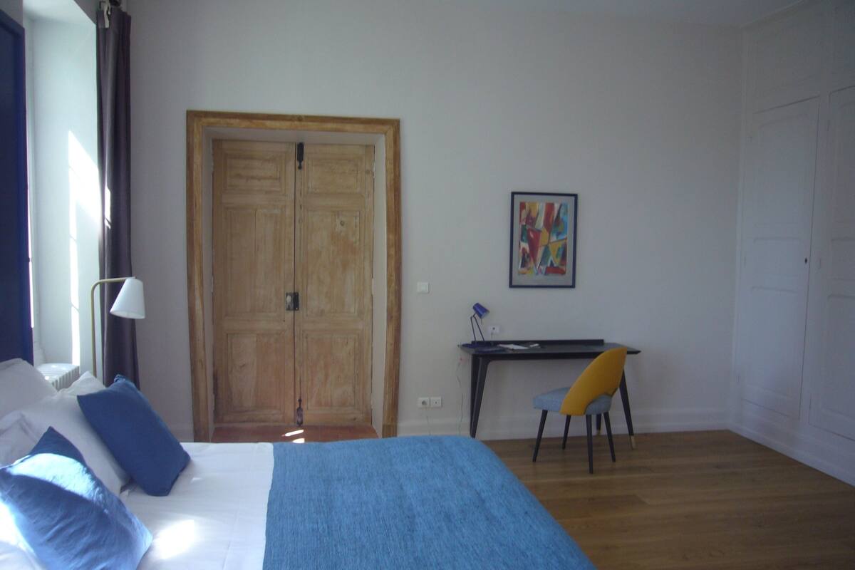 A bedroom with a bed, a desk, a chair, and a door.