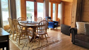 Een gezellig interieur van een chalet met een houten eettafel, stoelen, een bank en een divan.