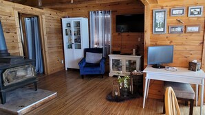 Een knus houten interieur met een blauwe fauteuil, een witte kast, een televisie en ingelijste foto’s aan de muur.