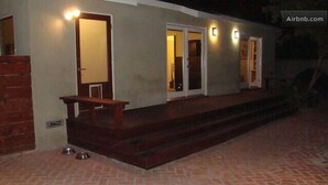 Un bâtiment doté d’une terrasse en briques, d’un banc en bois et d’une gamelle pour chien en métal.