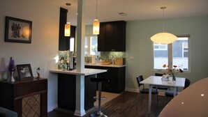 Une cuisine moderne avec des meubles de couleur sombre, un îlot central blanc, des luminaires suspendus et un coin repas comprenant une table et des chaises.