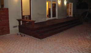 Un bâtiment doté d’une terrasse en briques, d’un banc en bois et d’une gamelle pour chien en métal.