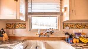 Una cocina con un ventanal amplio, un fregadero y distintos utensilios de cocina sobre la encimera.