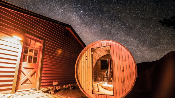 Una cabaña de madera con interior circular, una terraza de madera y un cielo nocturno estrellado.