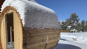 Una sauna de madera con puerta de vidrio, rodeada de nieve.