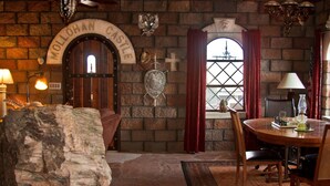 A rustic room with a stone wall, a wooden door labeled "MOLLON CASTLE," a shield emblem, and a window with red curtains.