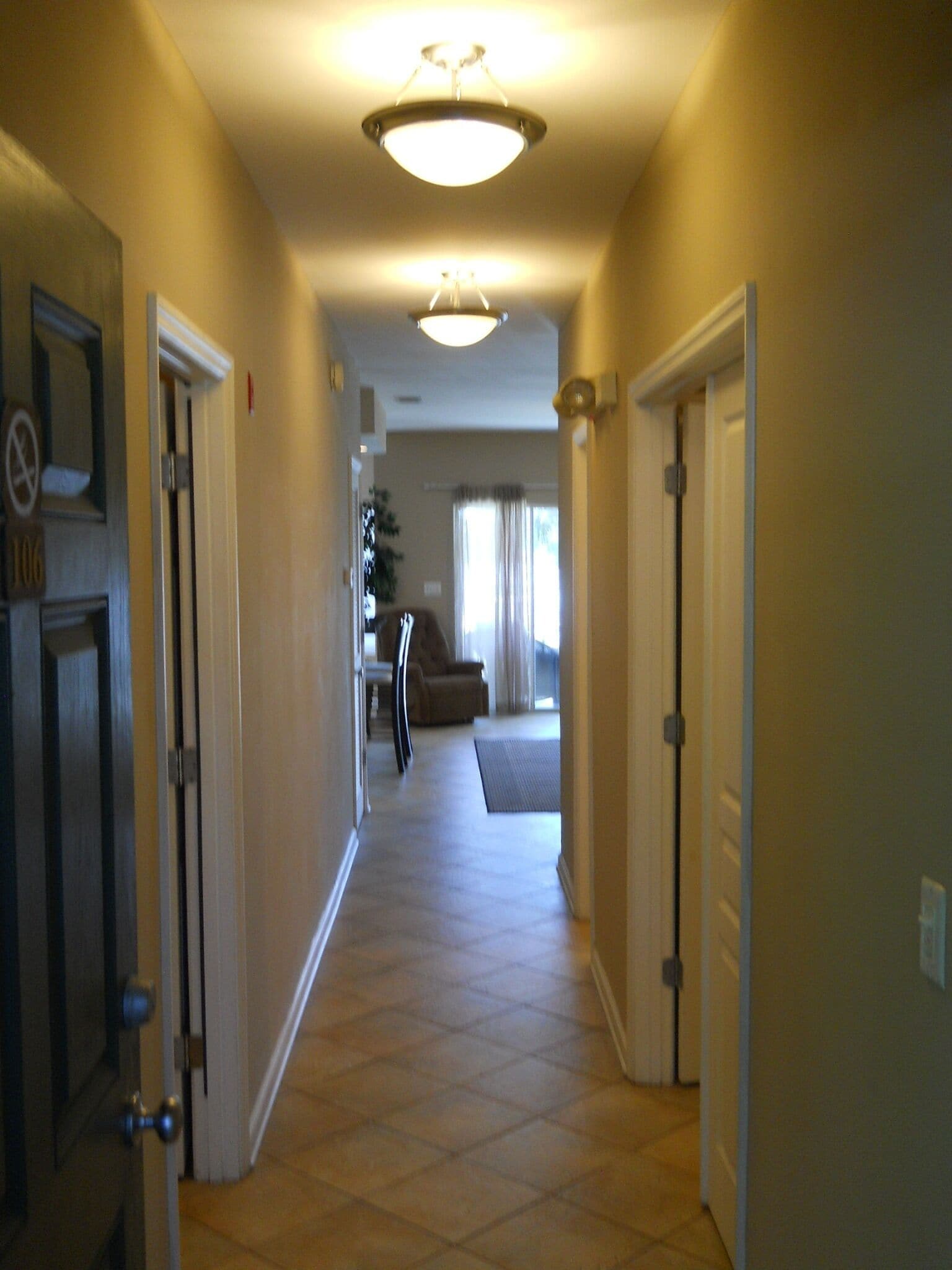 A hallway with a carpeted floor, a ceiling light, and a door on the left.