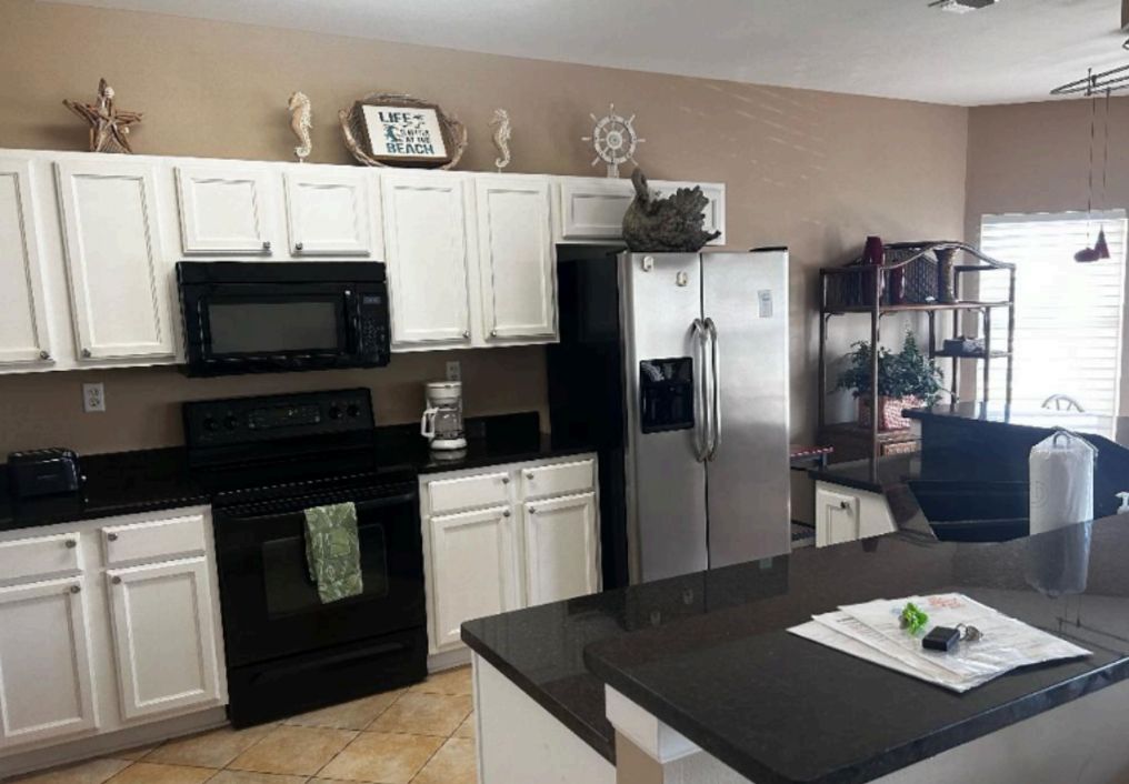Una cocina con armarios blancos, estufa negra, refrigerador de acero inoxidable y cafetera.