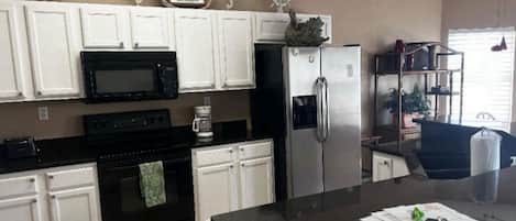 A kitchen with white cabinets, a black stove, a stainless steel refrigerator, and a coffee maker.