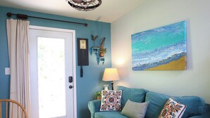 A room with a teal-colored sofa, a door with a view, a lamp, and a painting on the wall.