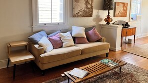 Un salon avec un canapé beige, une table basse en bois et un tapis à motifs. Des tableaux abstraits ornent le mur, et une lampe est posée sur une table d’appoint.