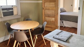 Une pièce avec une table ronde en bois, quatre chaises, un lit avec une literie à rayures et une porte en bois.