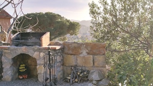 Un espace barbecue en pierre avec une pancarte indiquant « RBON GRILL » et un mur de pierre contre lequel sont empilés des bûches.