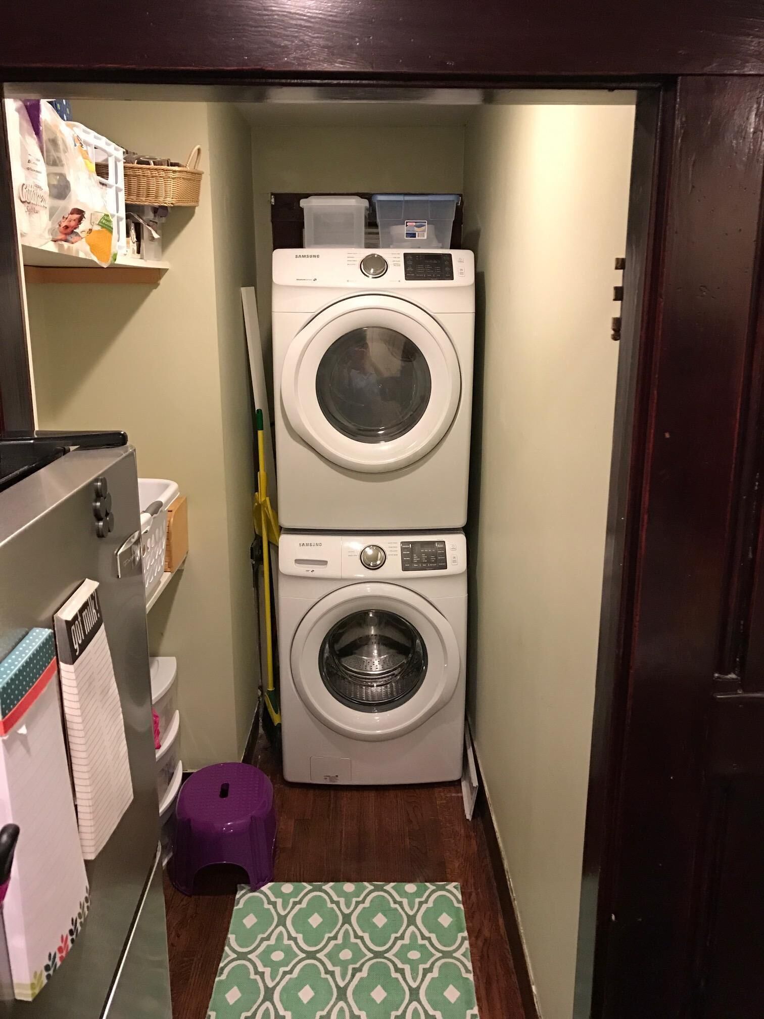 A compact laundry room with two stacked washing machines, a small stool, and a patterned mat on the floor.