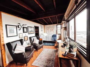 Una habitación acogedora con cama, escritorio, silla y sofá. Hay cuadros en la pared y una ventana con vistas.