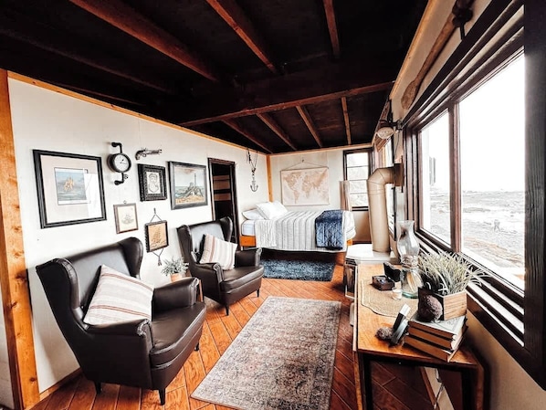 Una habitación acogedora con cama, escritorio, silla y sofá. Hay cuadros en la pared y una ventana con vistas.