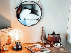 Una habitación acogedora con un espejo redondo, una lámpara antigua, un libro titulado 'Moses the Kitten', una mesa de madera y un horno rústico.