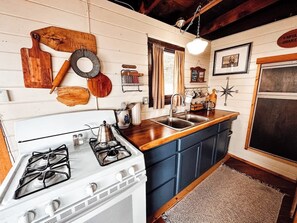 A kitchen with a white stove, wooden countertops, blue cabinets, and a rustic decor including a wooden cutting board, a metal strainer, and a vintage coffee grinder.
