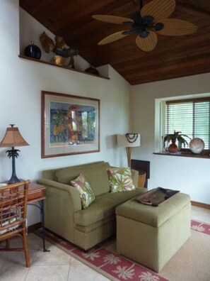 Un salon avec un canapé, un pouf et un ventilateur de plafond.