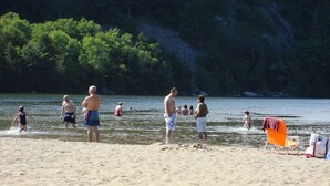 Una platja amb persones nedant i de peu a l'aigua. Hi ha cadires i una tovallola a la sorra.