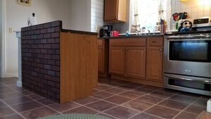 Una cuina amb armaris de fusta, una paret decorativa de maó, un forn d'acer inoxidable i una finestra amb cortines.