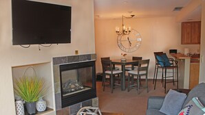 Ein Wohnzimmer mit Kamin, Fernseher, Essbereich mit Stühlen und einer Küche im Hintergrund.