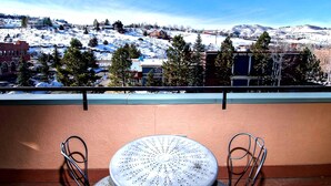 Ein Balkon mit Tisch und Stühlen, der auf eine verschneite Landschaft mit Gebäuden und Bäumen blickt.