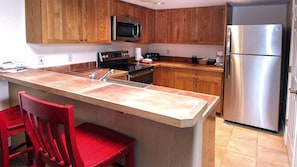 Una cocina con gabinetes de madera, un refrigerador de acero inoxidable, un microondas y una silla roja.