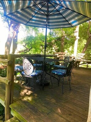 Relax on the patio surrounded by trees, with a shaded table and comfortable seating.