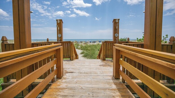 A wooden boardwalk leading to a beach with a clear sky.