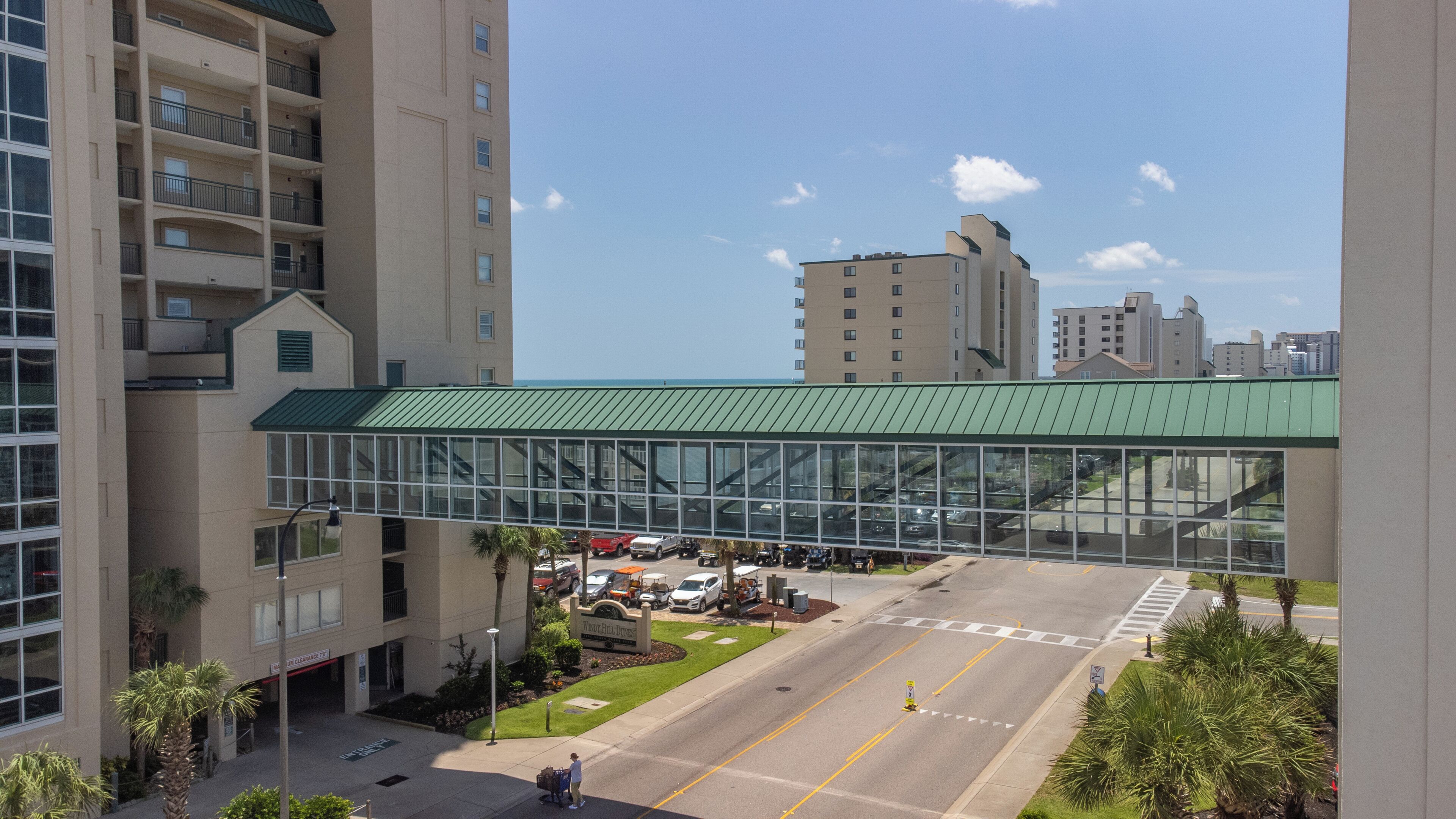 A modern building with a glass entrance and a green roof, surrounded by parking and greenery.
